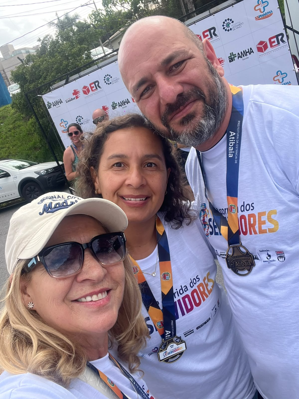 Servidores sorrindo com medalhas no painel de patrocinadores